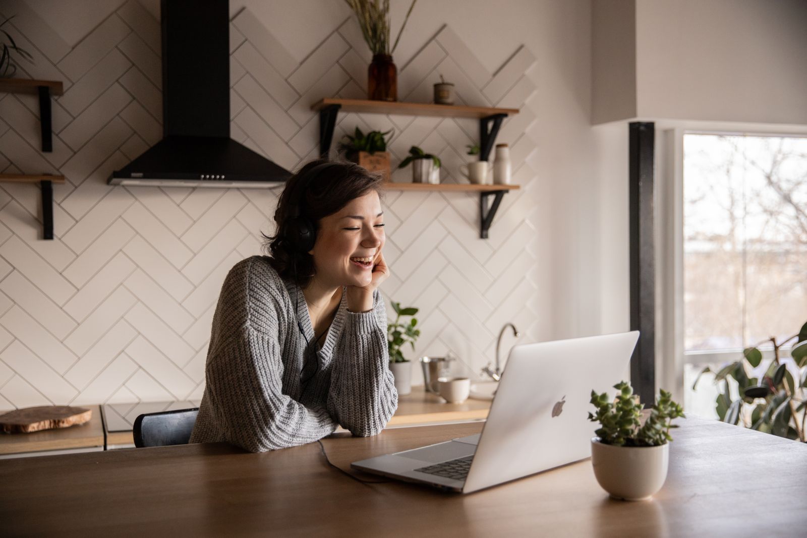 A smiling woman on a laptop call in a bright kitchen