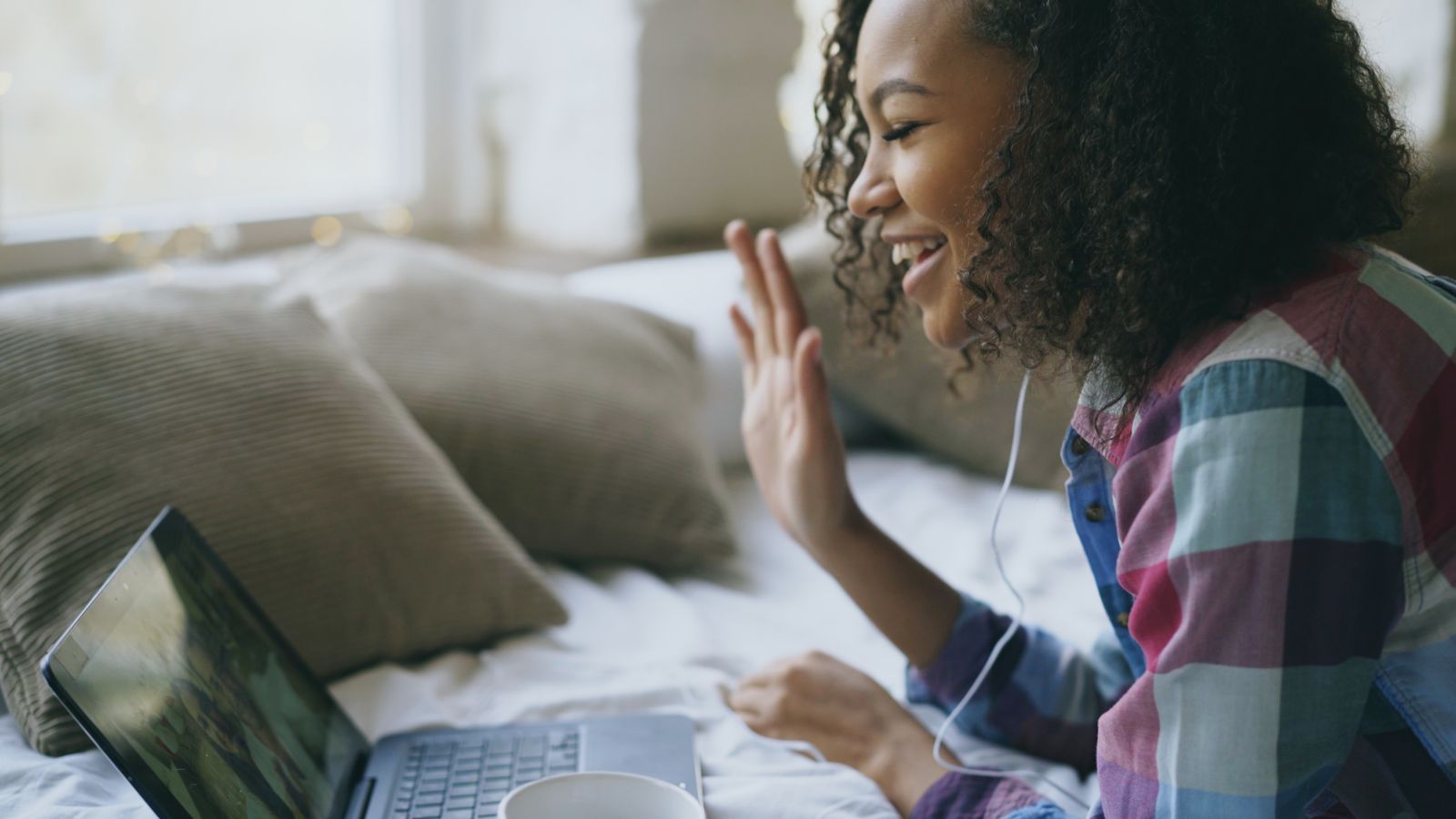 A smiling woman waving at her laptop during a video call
