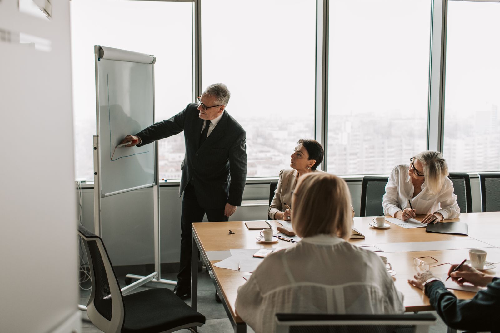 A grey-haired man in a suit drawing on a whiteboard for his team